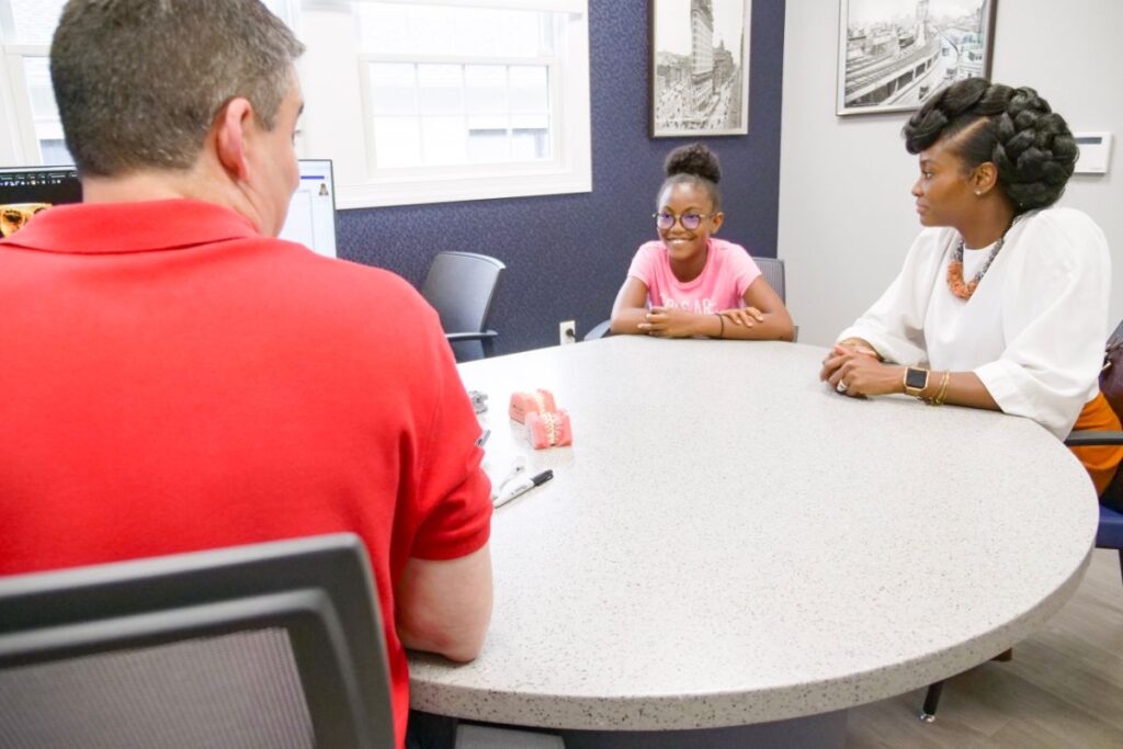 Dr. Gabriel Ollins goes over a treatment plan with a smiling young patient and her mother at the consultation table at Ollins Orthodontics, Nutley, NJ